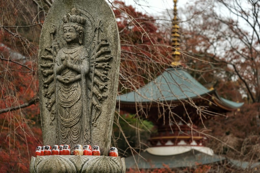 Des daruma sur une statue devant la pagode du Katsuo-ji de Minoh