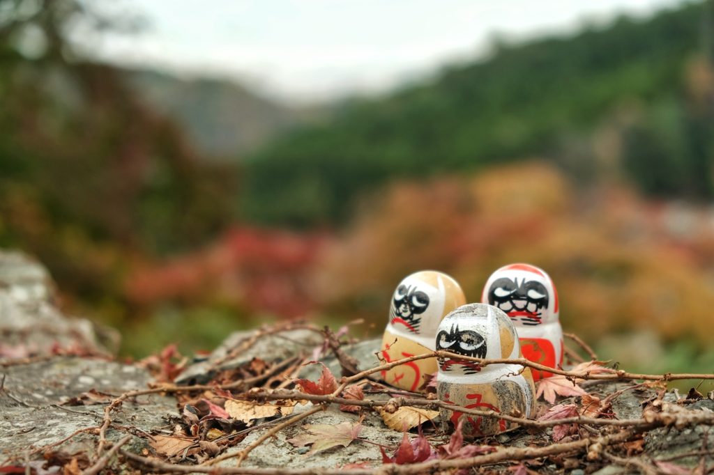 Des daruma sur un muret devant les montagnes autour du Katsuo-ji
